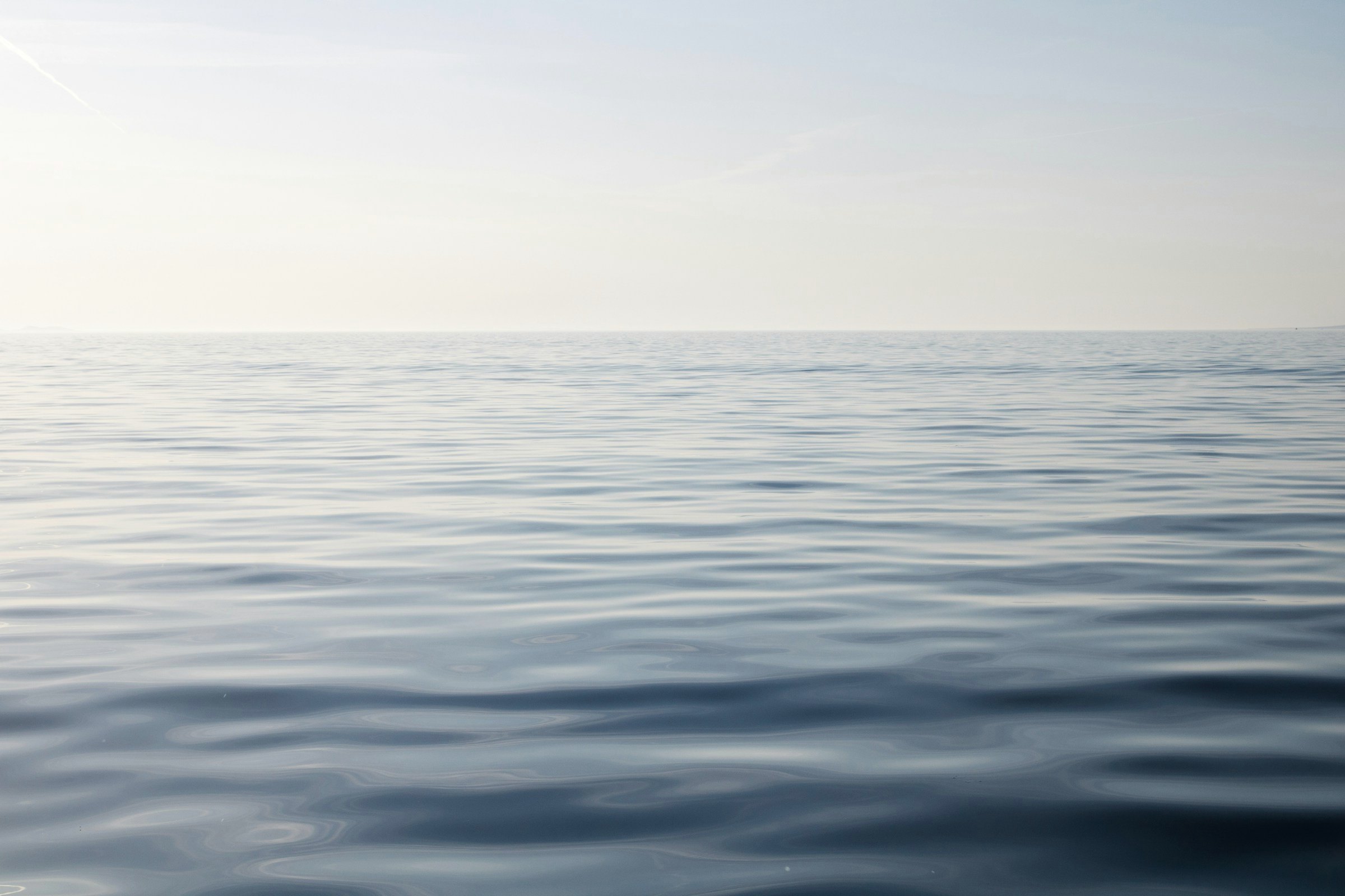 A silver sea under a bright sky, calm to the horizon